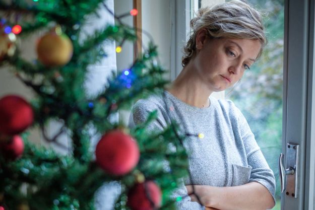 a woman looks at a christmas tree as she wonders is the holiday season the hardest time to get sober before entering an alcohol addiction treatment program in new hampshire